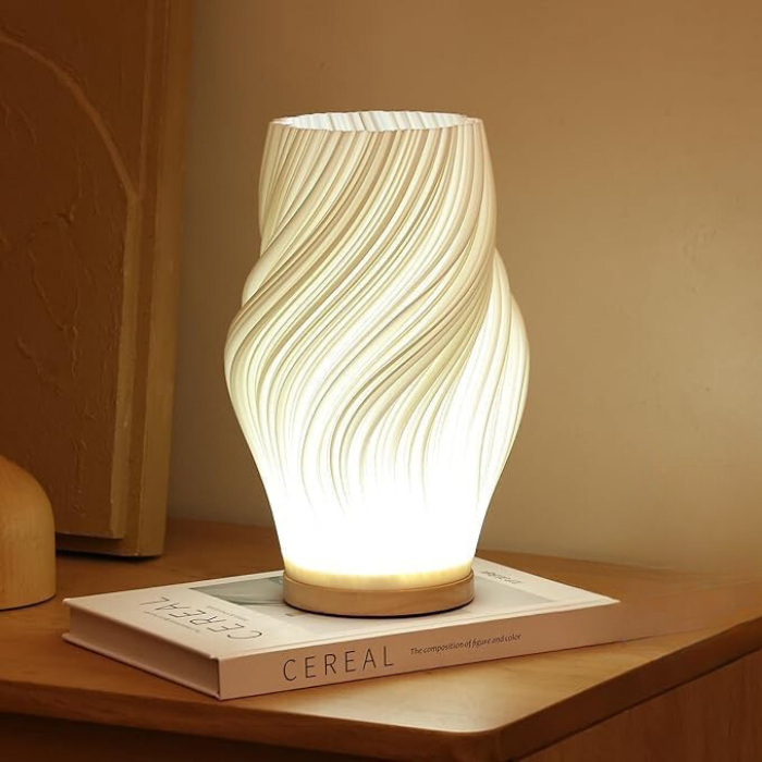 De Balaara Serene Wavecrest Lamp straalt een zacht, kalmerend licht uit en is geplaatst op een stijlvol boek, waardoor het een rustgevende en elegante sfeer toevoegt aan de ruimte.
