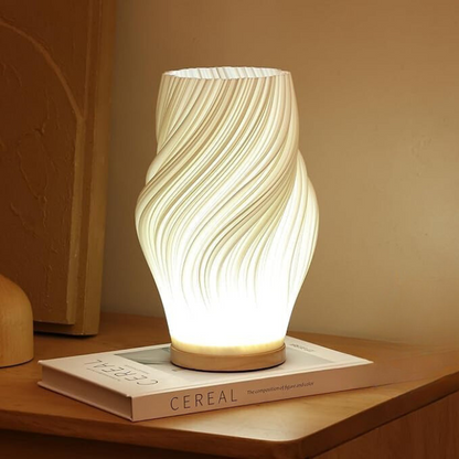 De Balaara Serene Wavecrest Lamp straalt een zacht, kalmerend licht uit en is geplaatst op een stijlvol boek, waardoor het een rustgevende en elegante sfeer toevoegt aan de ruimte.