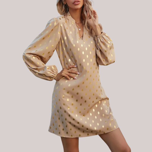 De Bellara Luxe jurk, een stijlvolle beige jurk met glanzende goudkleurige accenten en elegante lange mouwen. Deze verfijnde jurk combineert comfort met een chique uitstraling, perfect voor speciale gelegenheden.