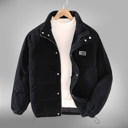 De Borealis winterjas in zwart corduroy is een perfecte combinatie van comfort en warmte. Deze gewatteerde jas heeft een praktische ritssluiting en drukknopen, evenals een subtiele merkpatch op de borst. Het ontwerp is casual en biedt optimale bescherming tegen de kou, ideaal voor dagelijks gebruik in de winter. De jas heeft een verstelbare onderrand en is zowel stijlvol als functioneel.