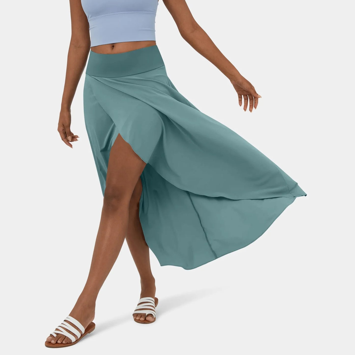 Een vrouw draagt een stijlvolle, roestbruine rok die elegant meebeweegt terwijl ze loopt. De rok heeft een hoge taille en een wijd uitlopende snit die zich mooi vormt tijdens het bewegen. De vrouw draagt een lichtblauw sporttopje en witte sandalen, wat een frisse, casual uitstraling geeft.