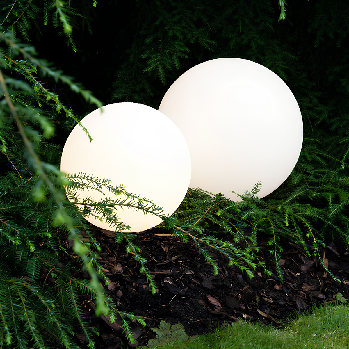 Twee witte sferische tuinlampen verlichten een groene tuin, gedeeltelijk bedekt door takken van bomen.