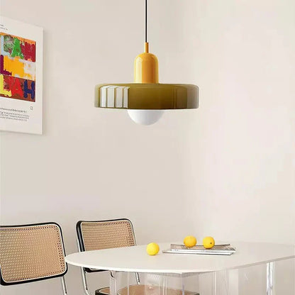 De Luminezza Living hanglamp in kleurrijk design hangt boven een minimalistische witte eettafel, omlijst door stijlvolle rotan stoelen. De geelgroene kap en speelse tinten van de lamp voegen een warme en moderne sfeer toe aan de ruimte, perfect voor een eigentijdse eetkamer.