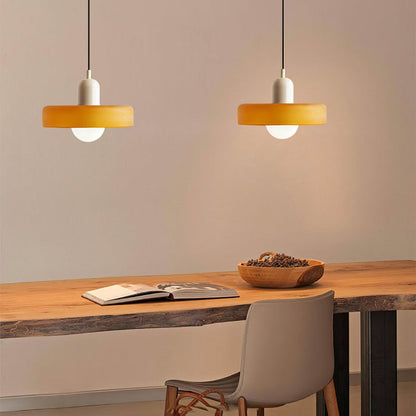 Twee Luminezza Living hanglampen in een kleurrijk design met warme gele kappen en elegante witte fittingen. Ideaal om een gezellige en stijlvolle ambiance te creëren boven een houten tafel in een moderne eet- of werkruimte.