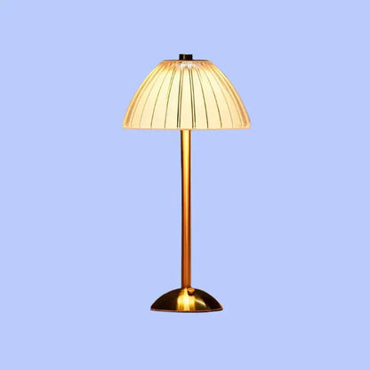 Een moderne draadloze tafellamp met een gouden voet en een geplooide stoffen lampenkap die een zachte, warme gloed uitstraalt. Het elegante ontwerp voegt een verfijnde toets toe aan elke kamer, perfect voor het creëren van een gezellige sfeer.