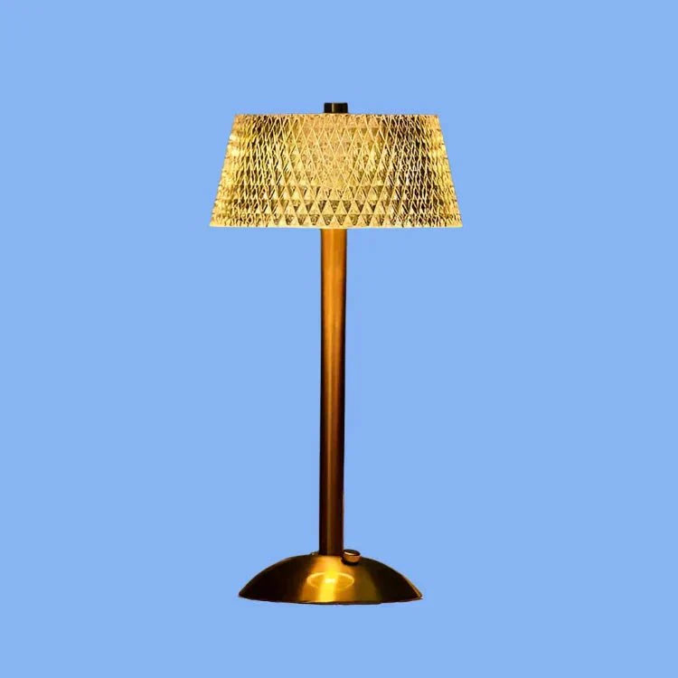Een moderne draadloze tafellamp met een slanke gouden voet en een getextureerde, geometrisch patroon lampscherm dat een zachte, warme gloed uitstraalt, wat een elegante touch toevoegt aan de inrichting van elke kamer.