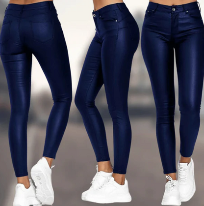 Een vrouw draagt een elegante, donkerblauwe, hoog-taille broek van Onyx met een strakke pasvorm. De broek heeft een subtiele glans en is gecombineerd met een paar witte sneakers voor een moderne, casual look.