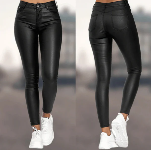 Een vrouw draagt een strakke, zwarte, hoog-taille broek van Onyx met een leren uitstraling. De broek heeft een moderne en elegante pasvorm, perfect gecombineerd met witte sneakers voor een trendy en comfortabele look