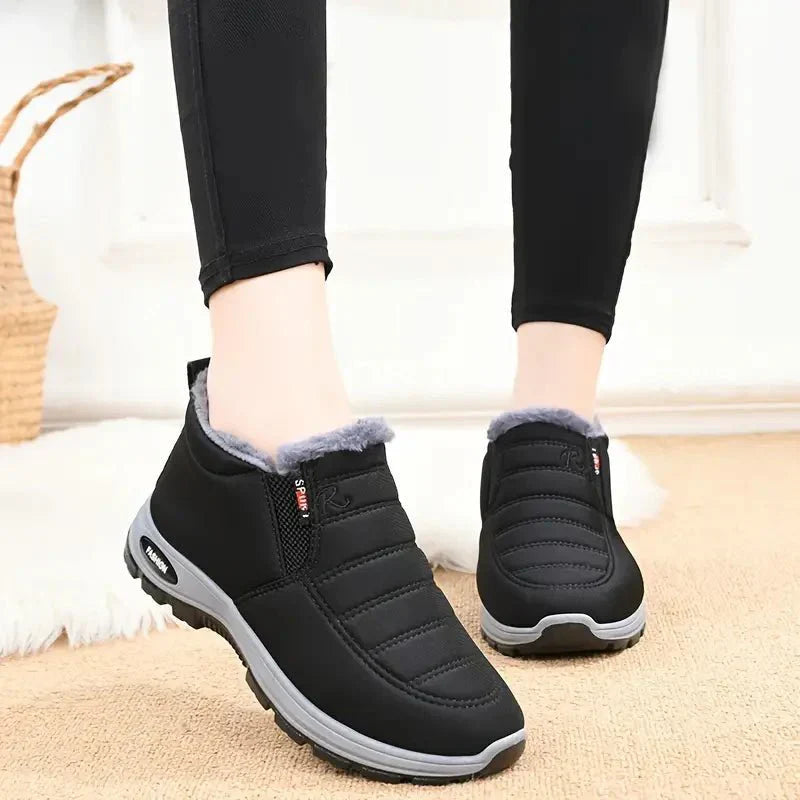 Zwarte Tessura schoenen met een zachte, warme voering rond de enkels, ontworpen voor comfort en warmte in de koude maanden. De schoenen hebben een sportieve uitstraling met een grijze zool en zijn ideaal voor dagelijks gebruik.